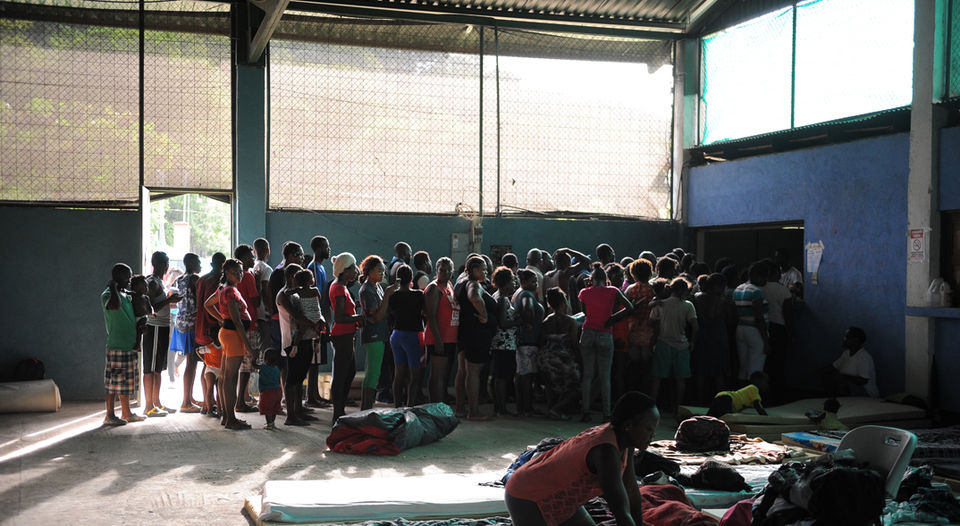 Decenas de migrantes, en su mayoría haitianos, hacen fila para recibir un plato de comida en el albergue que el gobierno instaló en un gimnasio en El Jobo, a unos 16 kilómetros del centro de La Cruz, en Guanacaste. (Fotografía: Jeffrey Zamora)